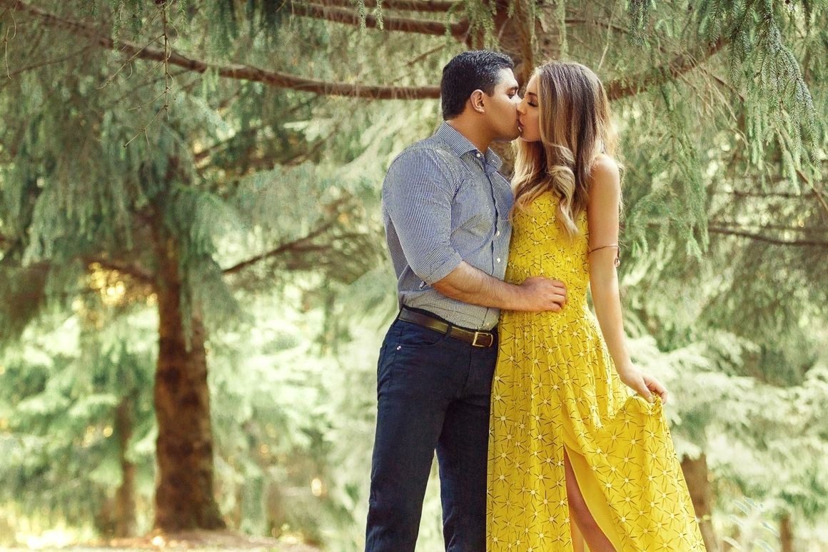 A man and woman kissing in front of trees.