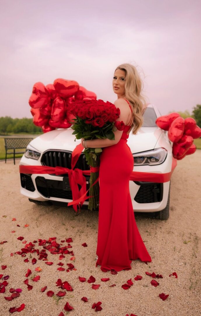 A woman in red holding roses next to a car.