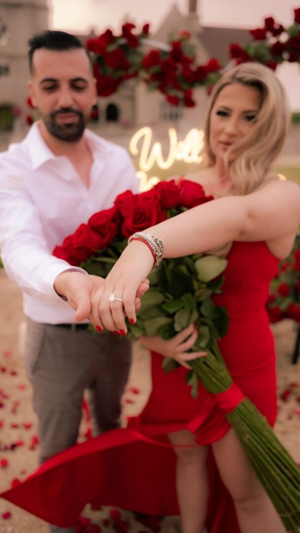 A man and woman holding roses in front of a sign.