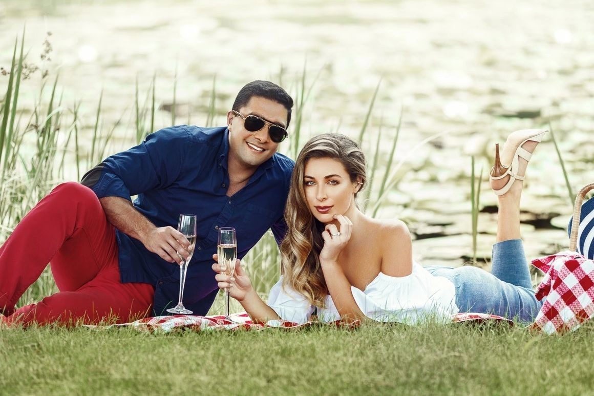 A man and woman sitting on the grass with wine glasses.