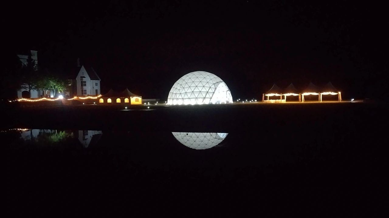 A large sphere lit up at night by lights.