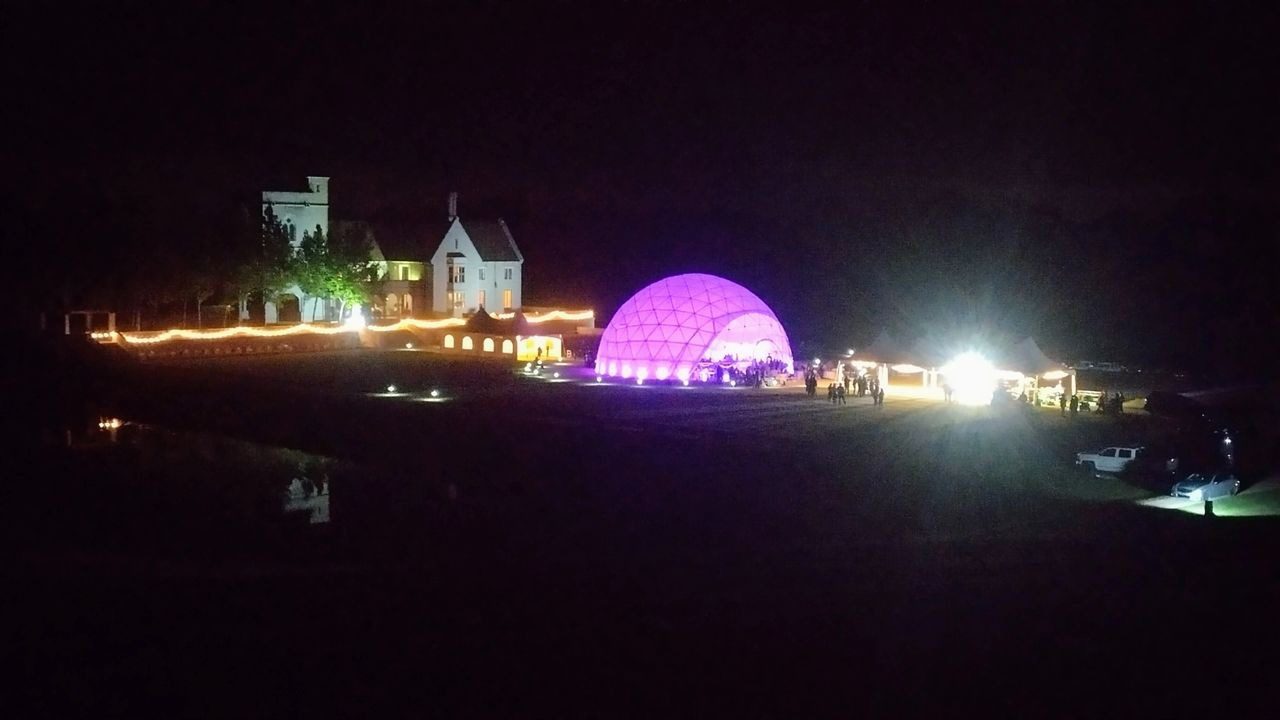A large purple dome is lit up at night.