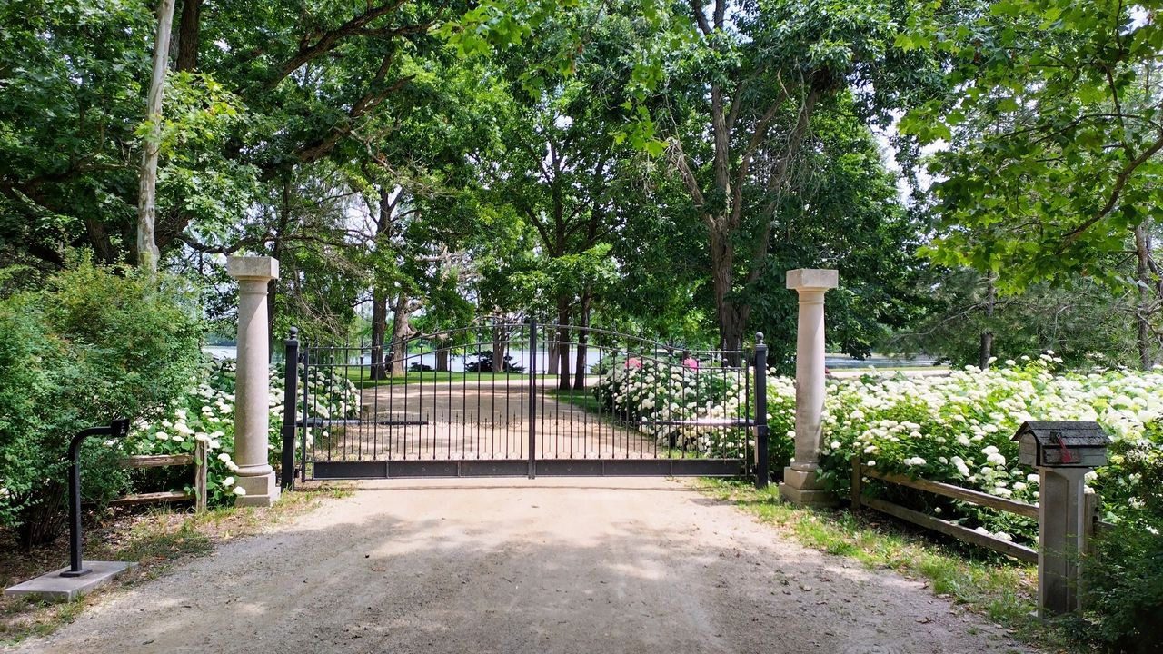 A gated driveway with trees and bushes in the background.