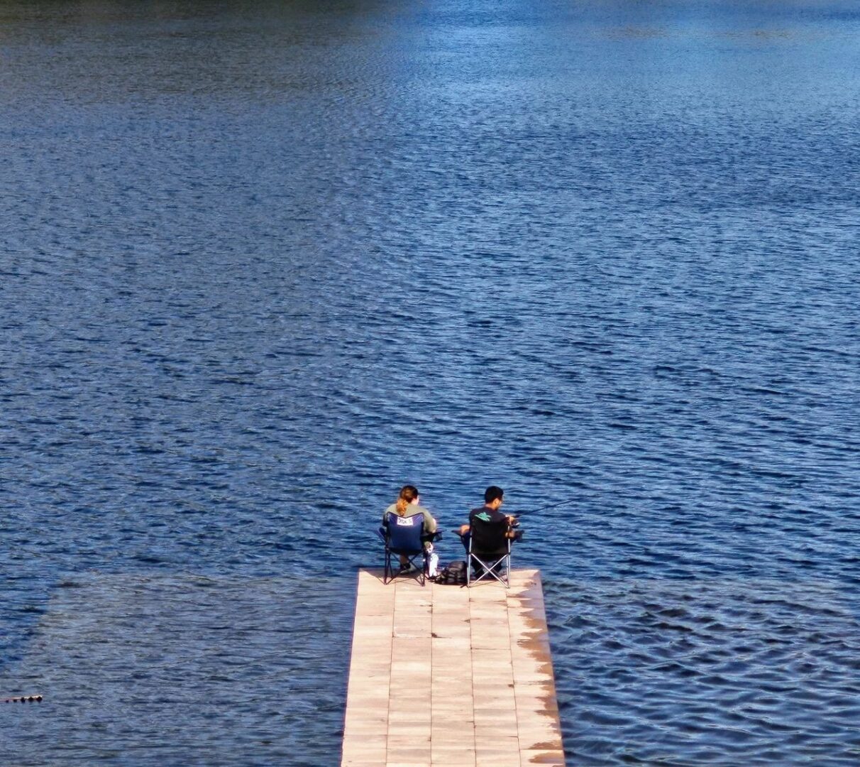 Two people sitting on a pier in the middle of water.