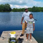 A man and boy standing on the dock of a lake.
