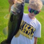 A boy holding a large fish in his hand.