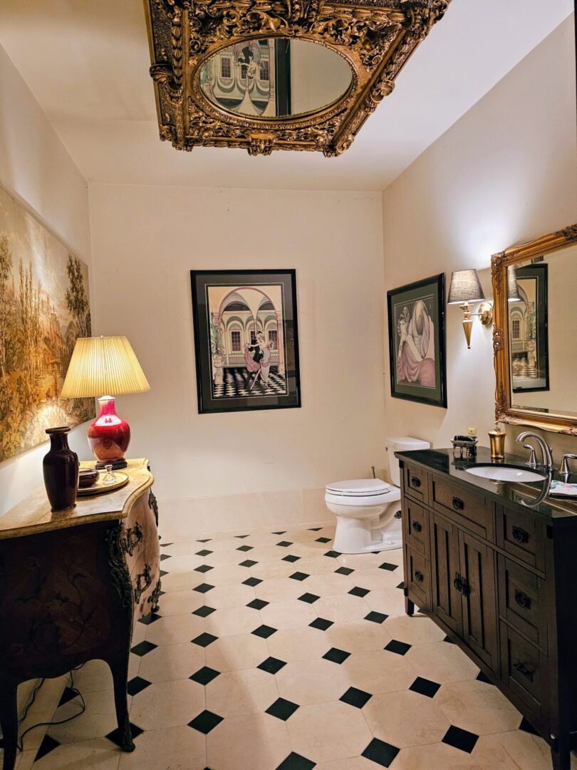 A bathroom with black and white tile floor, two sinks, mirror, toilet and vanity.