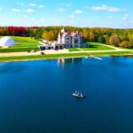 A large mansion beside a lake with a boat on the water.