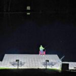 Person standing alone on a large rooftop at night.