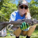 Smiling woman holding a large fish outdoors.