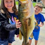 Two kids proudly hold a giant fish they caught.