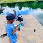 Child fishing with a rod near a lake on a sunny day.