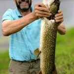 A man proudly holds a large fish he caught outdoors.