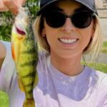 A woman wearing sunglasses proudly holding a yellow and black striped fish.