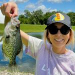 Smiling woman holds up a large fish she caught outdoors.