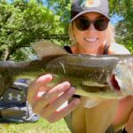 Woman holding a freshly caught fish outdoors, smiling.