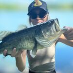 Person holding a large bass fish with a lake background.