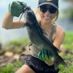 Woman holding a large fish she caught, smiling outdoors.