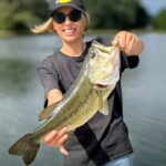 Person proudly holding a large fish by the water.