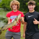 Two boys proudly holding a large fish outdoors.