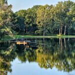 A serene lake with a wooden dock surrounded by lush green trees.