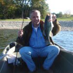 Man proudly holding a large fish on a boat in a lake.