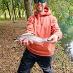 Man holding a freshly caught fish by a riverside in autumn.