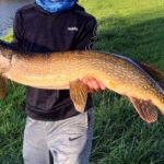Person holding a large fish outdoors on grass.
