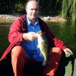 Man in red jacket holding a large fish on a boat.