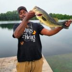 Man proudly holding a large fish by a lakeside.