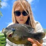 Woman wearing sunglasses holding a large fish outdoors.