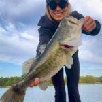 Woman proudly holding a large bass fish she caught.