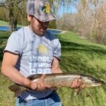 Man holding a large fish outdoors on a sunny day.