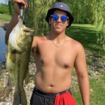 Young man proudly holding a large fish outdoors.