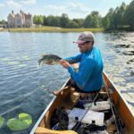 Man fishing from a canoe on a lake near a castle.