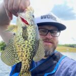Man holding a speckled fish near a lake.