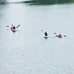 Three kayakers paddling on a calm lake.