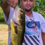 Man proudly holds a large bass fish he caught outdoors.