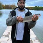 Man holding a freshly caught fish by a lakeside.