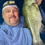 Man in blue shirt holding a large fish at night.