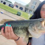 Person holding a large fish outdoors near buildings.