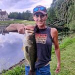 Person proudly holding a large fish by a water body.