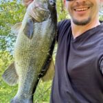 Man holding a large bass fish with a smile outdoors.