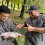 Two men happily holding and admiring a freshly caught fish outdoors.