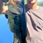 Person proudly holding a large fish against a blue sky.