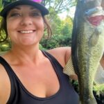 Woman smiling, proudly holding a large fish outdoors.