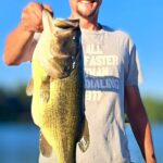 Man proudly holding a large fish caught from a lake.