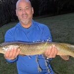 Man proudly holding a large fish outdoors.
