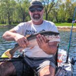 Man proudly holding a large bass fish on a sunny day.