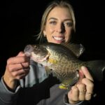 Woman proudly holding a large fish she caught at night.